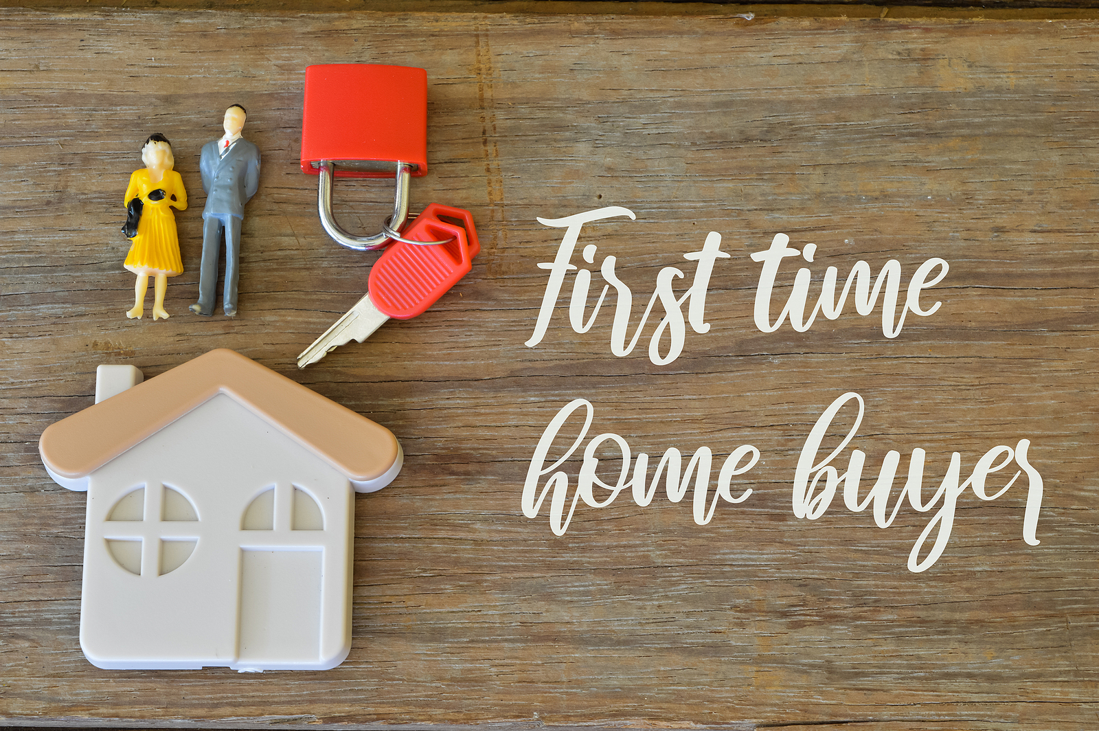 First-Time Home Buyer text, house block, keys, and a couple toy on a wooden table