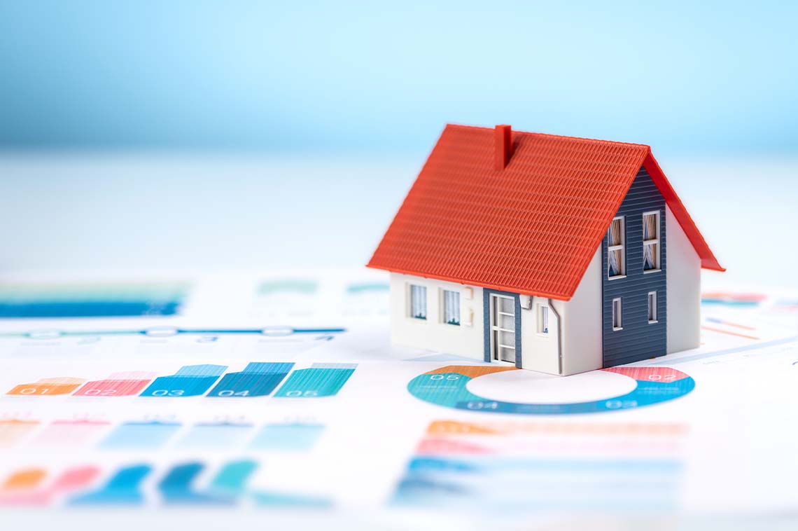 Mini house figurine on top of papers with graphs