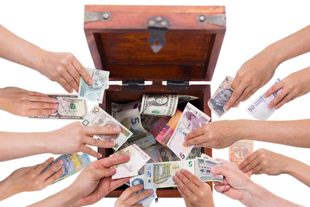 Several hands donating different currencies into a wooden box