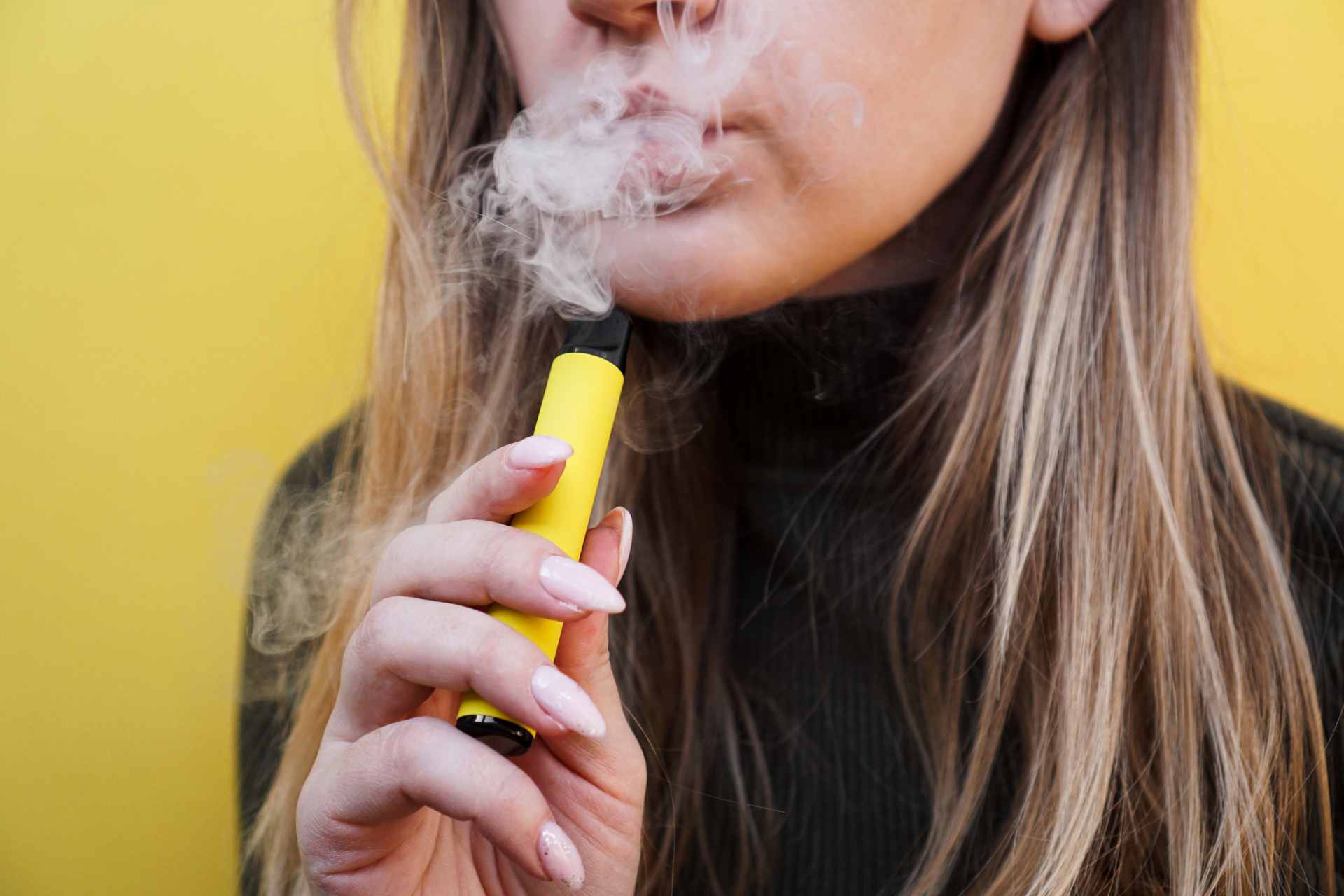 A woman using a yellow disposable vape