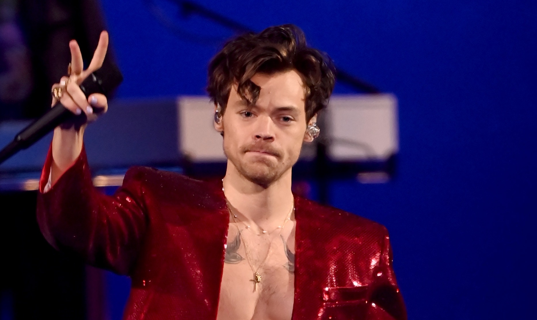 Harry Styles wearing a red coat while holding a mic