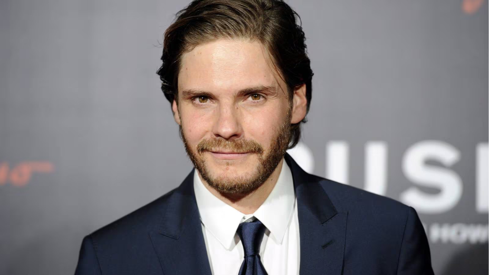 Daniel Brühl wearing a black suit and tie on a white shirt at an event