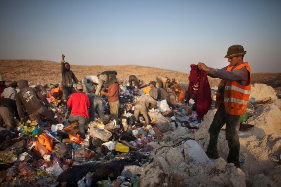 A group of people in a landfill picking out clothes 