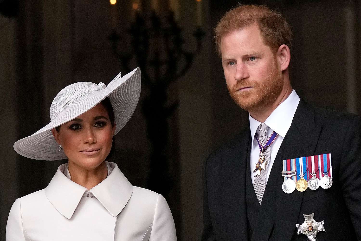 Meghan Markle wearing a white coat and hat and Prince Harry wearing a black suit with medals