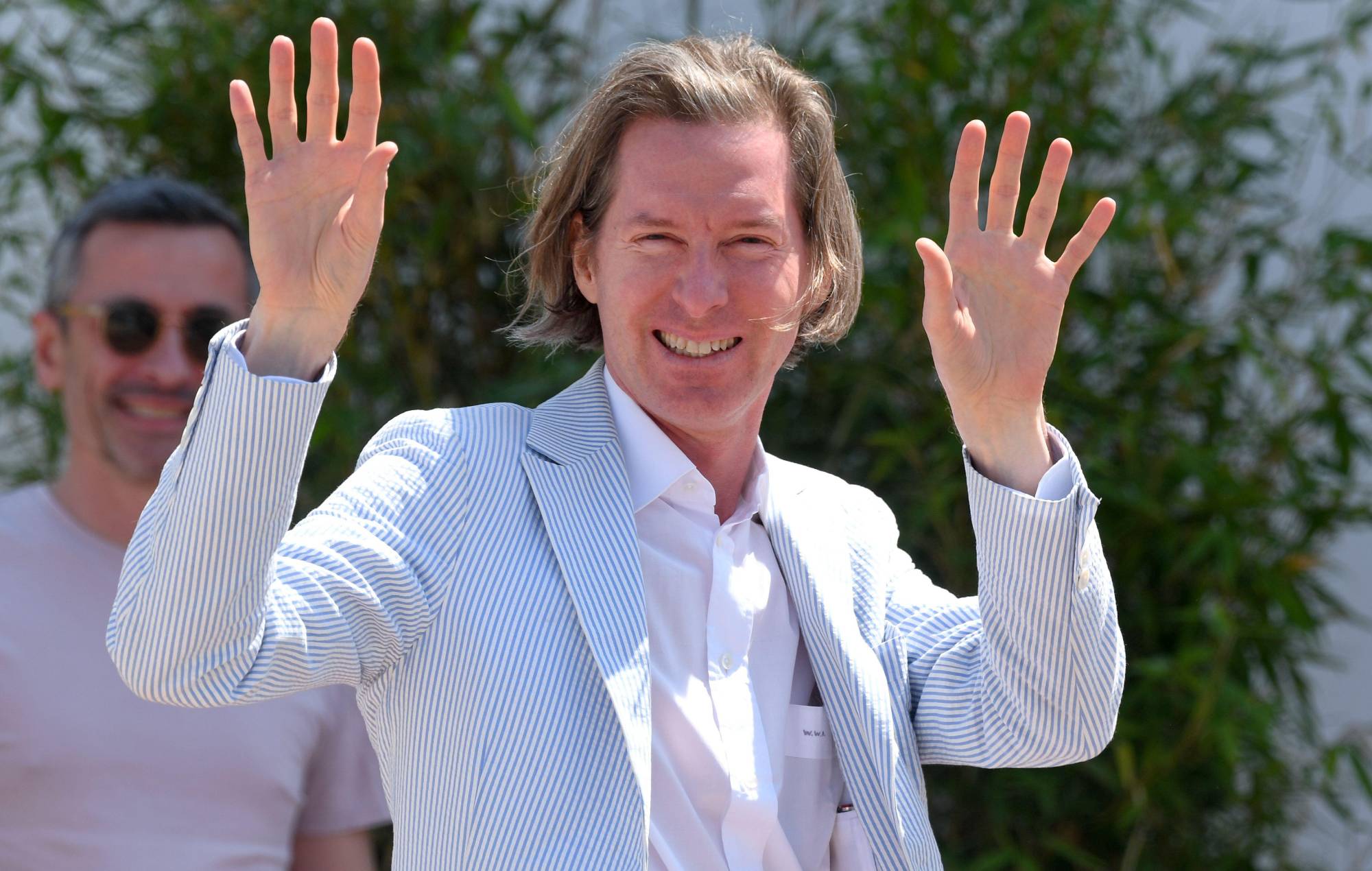 Wes Anderson wearing a stripe blue coat while waving his hands