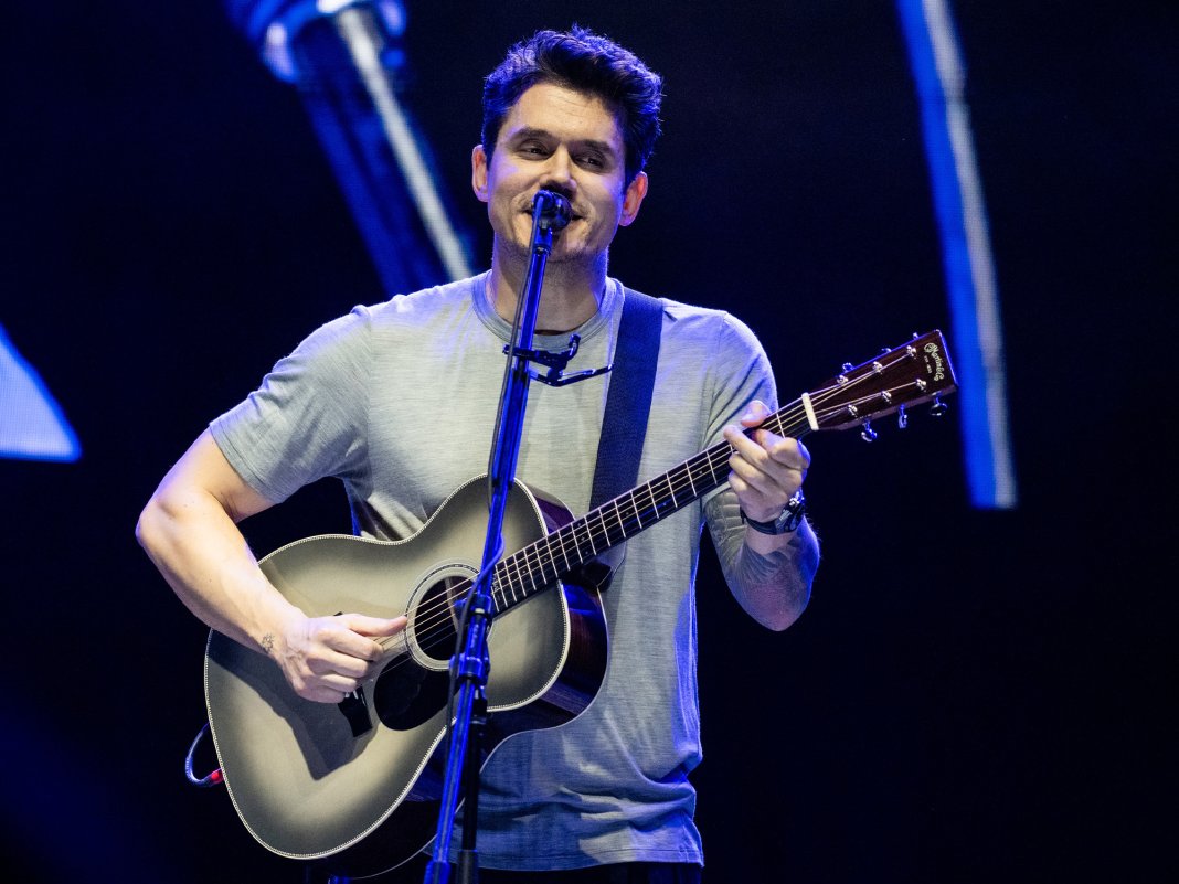 John Mayer wearing a gray shirt while playing a guitar