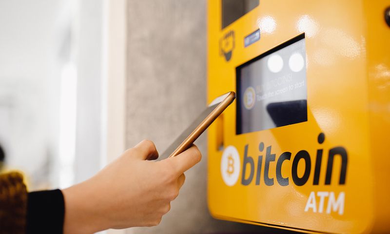 A man holding phone next to a Bitcoin ATM