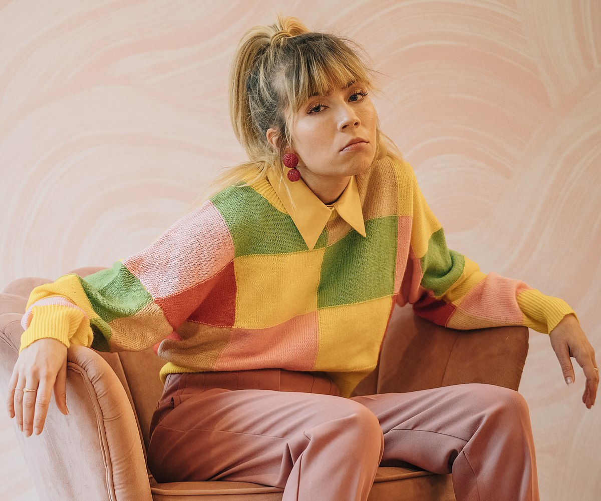 Jennette McCurdy wearing a colorful sweat shirt while sitting on a couch