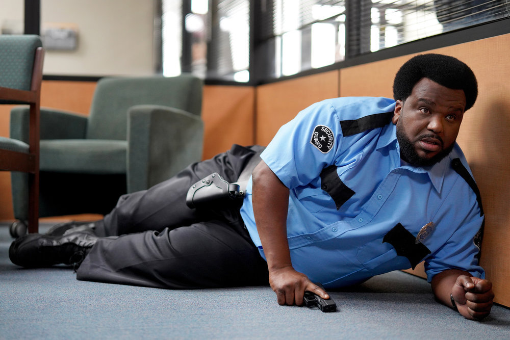 Craig Robinson wearing a police uniform while laying down in a movie scene