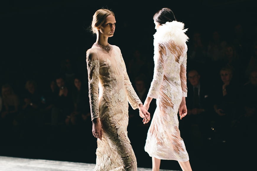 Two women walking on a runway while wearing a white dress