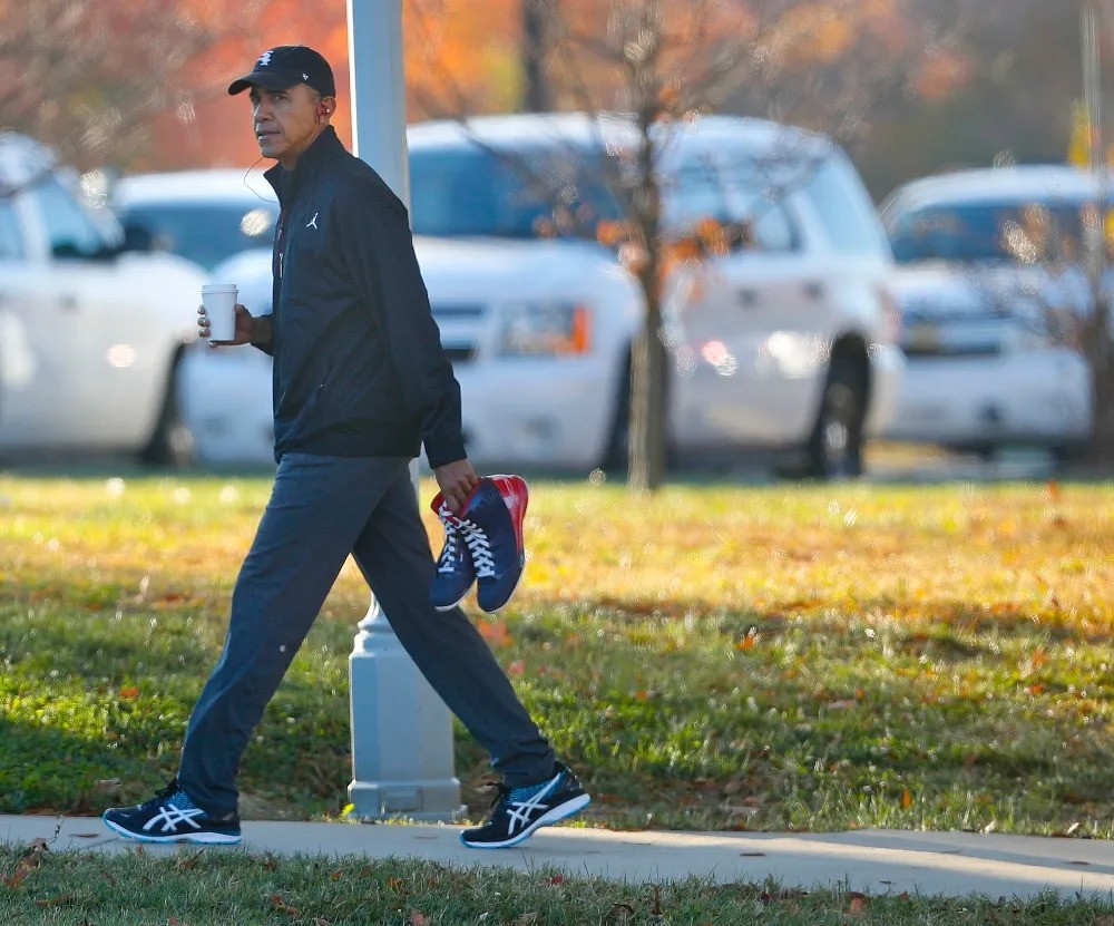 Barack obama walking down the road wearing a cap, sneakers and coffee while he listens to music