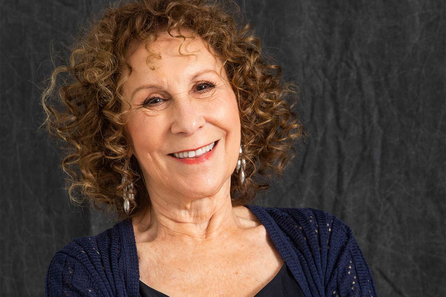 Rhea Perlman wearing a blue jacket with a smile