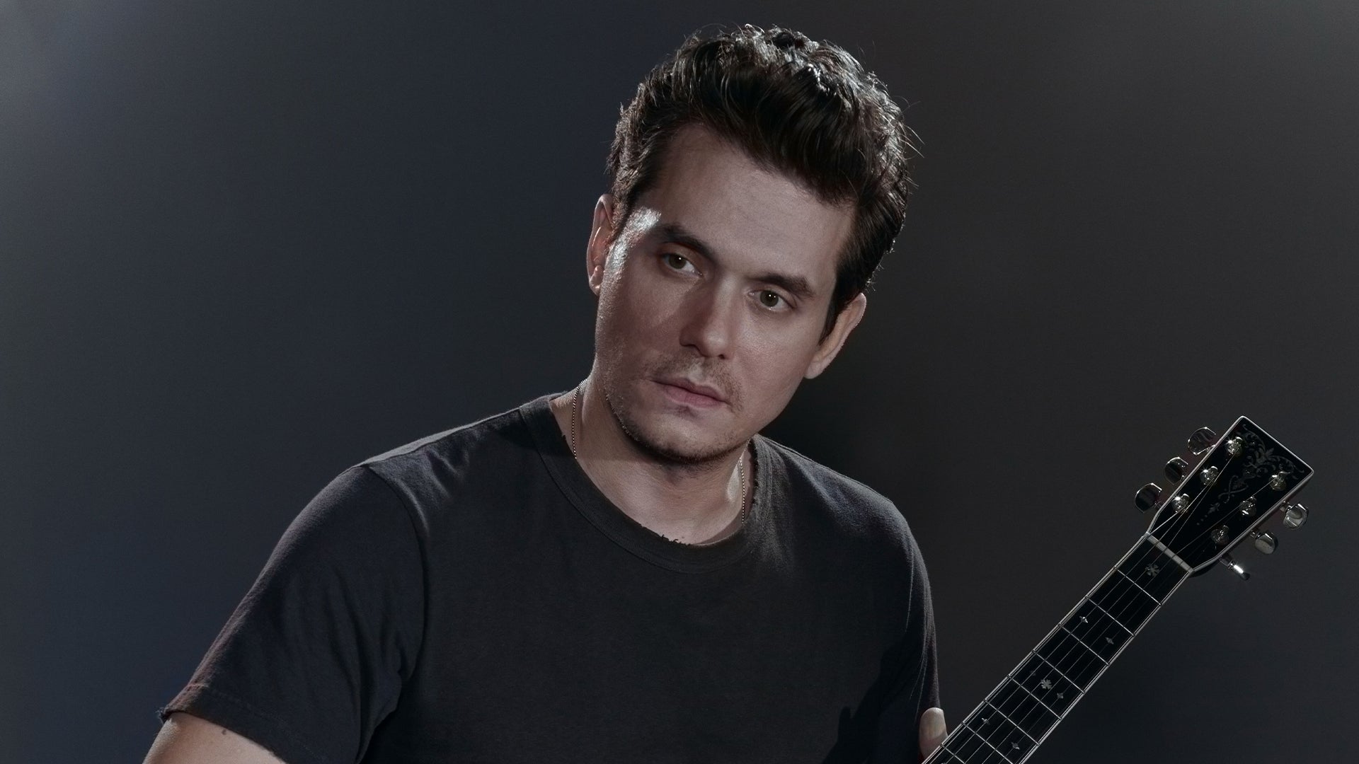 John Mayer wearing a black shirt while holding a guitar